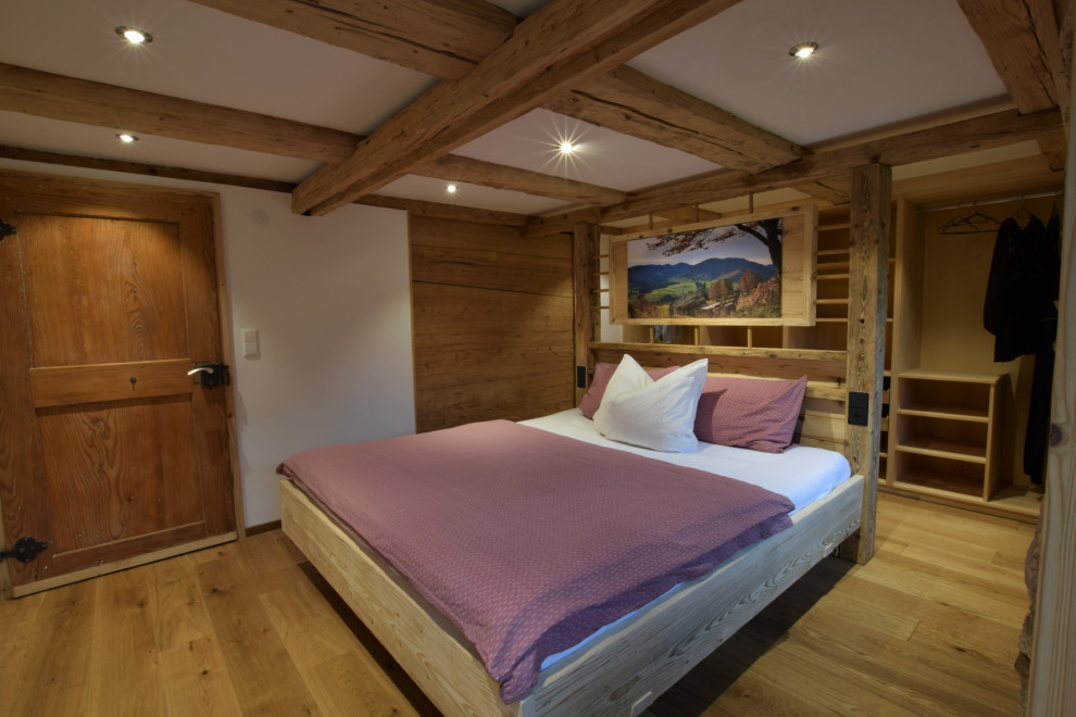 Mittelgroßes Uriges Hauptschlafzimmer mit weißer Wandfarbe, dunklem Holzboden, freigelegten Dachbalken und Holzdielenwänden in Sonstige