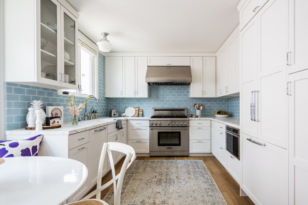 Small beach style u-shaped eat-in kitchen in San Francisco with shaker cabinets, white cabinets, marble benchtops, blue splashback, ceramic splashback, stainless steel appliances, medium hardwood floors, no island, beige floor and white benchtop.