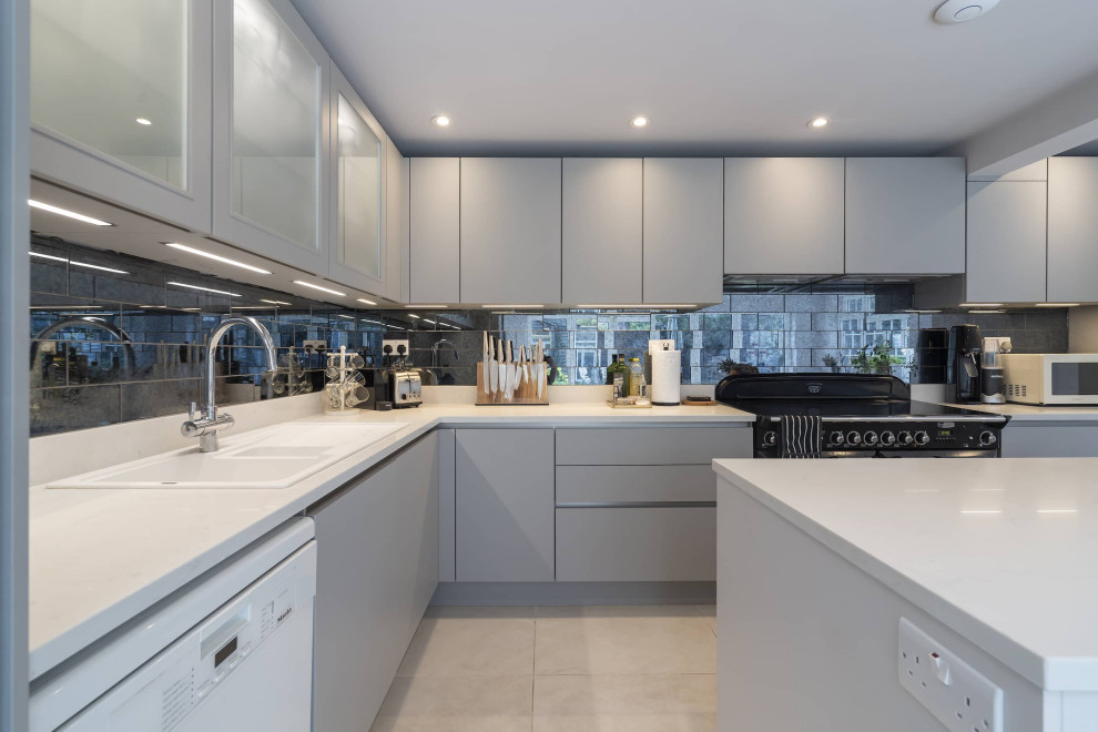 This is an example of a large contemporary grey and white l-shaped open plan kitchen in Oxfordshire with a built-in sink, glass-front cabinets, grey cabinets, quartz worktops, mirror splashback, ceramic flooring, an island, beige floors, white worktops, a drop ceiling and feature lighting.