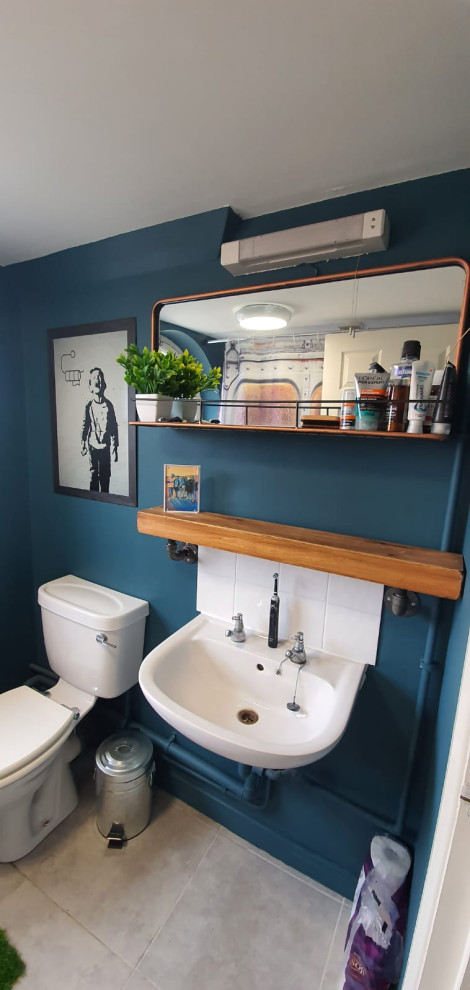This is an example of a small urban bathroom in Essex with a built-in bath, a shower/bath combination, a one-piece toilet, white tiles, blue walls, a pedestal sink, a shower curtain, a feature wall and a single sink.