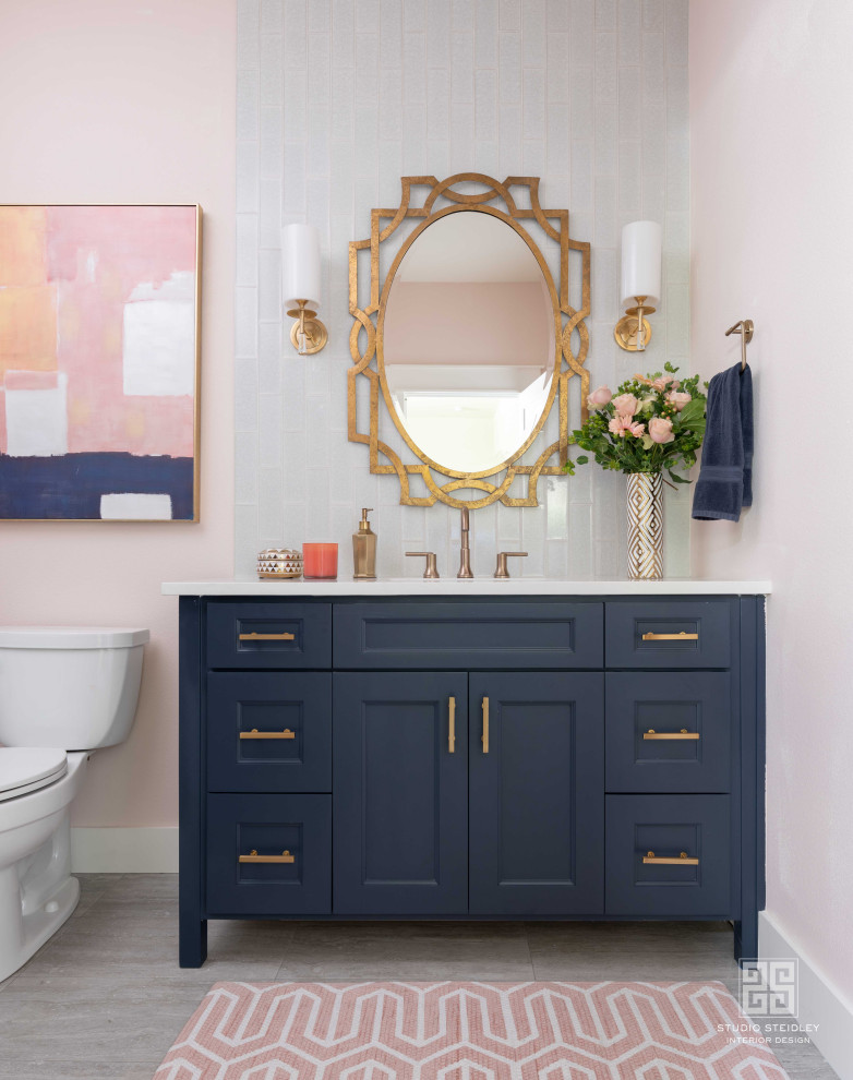 This is an example of a mid-sized asian 3/4 bathroom in Dallas with blue cabinets, an alcove tub, a shower/bathtub combo, a two-piece toilet, pink tile, subway tile, pink walls, porcelain floors, an undermount sink, granite benchtops, grey floor, a hinged shower door, white benchtops, a single vanity, a freestanding vanity and beaded inset cabinets.