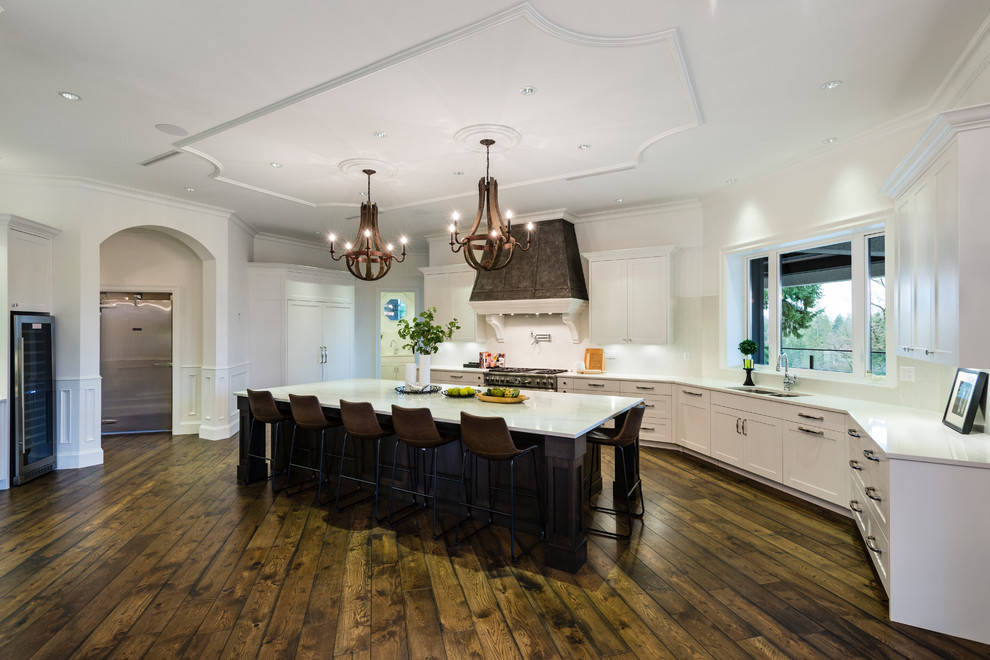 Inspiration for a huge rustic u-shaped medium tone wood floor and brown floor open concept kitchen remodel in Vancouver with an undermount sink, shaker cabinets, white cabinets, solid surface countertops, white backsplash, stone slab backsplash, stainless steel appliances, an island and white countertops