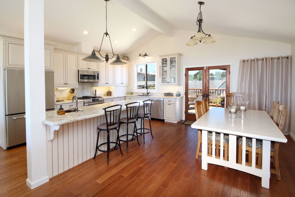 This is an example of a mid-sized country l-shaped eat-in kitchen in Other with an undermount sink, raised-panel cabinets, white cabinets, white splashback, stainless steel appliances, medium hardwood floors, with island and brown floor.