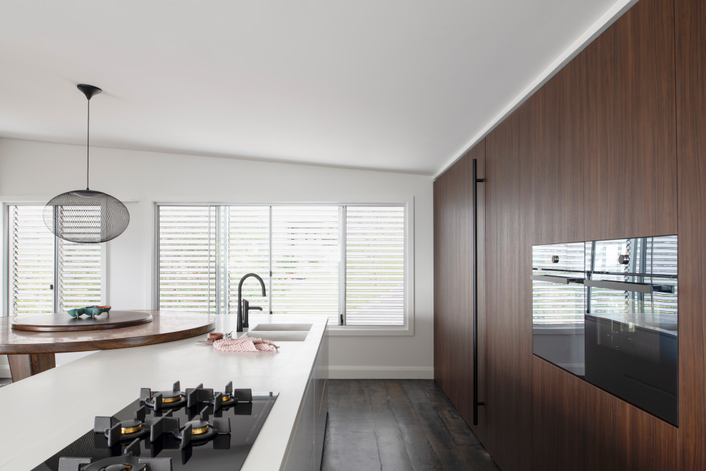 Example of a large trendy galley dark wood floor open concept kitchen design in Sydney with a double-bowl sink, flat-panel cabinets, white cabinets, solid surface countertops, black appliances, an island and white countertops