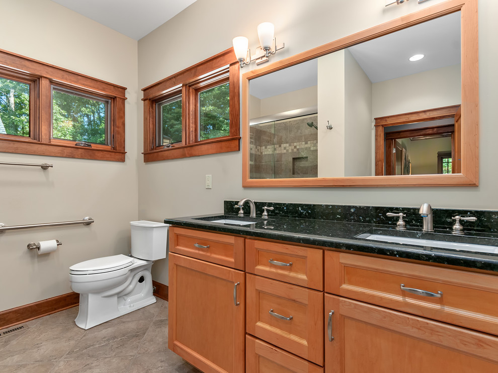 Mid-sized arts and crafts 3/4 brown tile porcelain tile and beige floor alcove shower photo with recessed-panel cabinets, medium tone wood cabinets, a two-piece toilet, beige walls, an undermount sink, granite countertops and black countertops