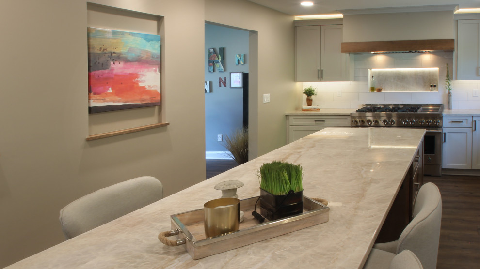 Eat-in kitchen - mid-sized transitional l-shaped brown floor eat-in kitchen idea with an undermount sink, shaker cabinets, white cabinets, quartzite countertops, white backsplash, ceramic backsplash, stainless steel appliances, an island and beige countertops