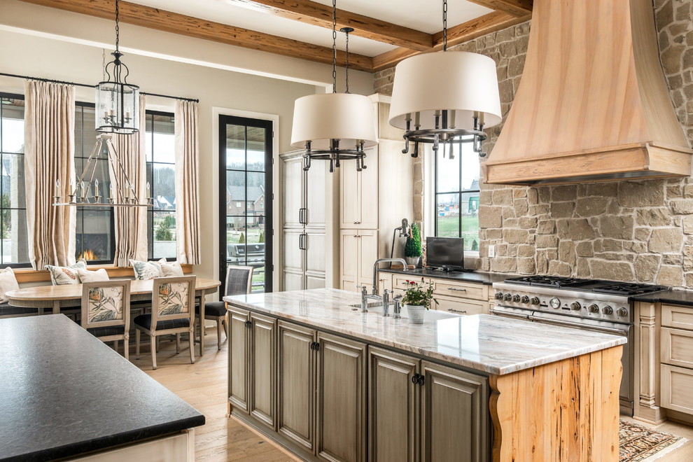 Design ideas for a traditional l-shaped eat-in kitchen in Nashville with a farmhouse sink, distressed cabinets, beige splashback, stainless steel appliances, multiple islands, raised-panel cabinets, stone tile splashback, medium hardwood floors, brown floor and beige benchtop.
