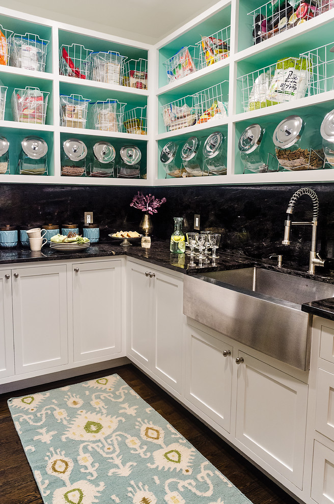 Photo of a transitional l-shaped kitchen pantry in New York with dark hardwood floors, granite benchtops, black splashback, stone slab splashback, a farmhouse sink, shaker cabinets and white cabinets.