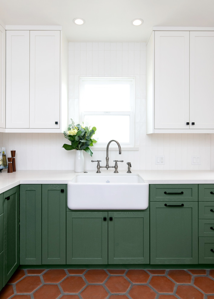 Inspiration for a mid-sized transitional l-shaped separate kitchen in Los Angeles with a farmhouse sink, shaker cabinets, green cabinets, quartz benchtops, white splashback, ceramic splashback, stainless steel appliances, terra-cotta floors, no island, brown floor and white benchtop.