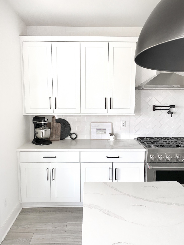 Design ideas for a large modern l-shaped eat-in kitchen in Seattle with an undermount sink, shaker cabinets, white cabinets, quartz benchtops, white splashback, porcelain splashback, stainless steel appliances, laminate floors, with island, grey floor and white benchtop.