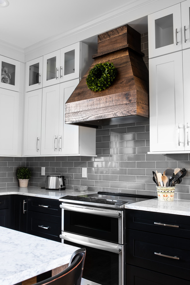 Inspiration for a mid-sized country l-shaped eat-in kitchen in Charlotte with a farmhouse sink, shaker cabinets, black cabinets, quartz benchtops, grey splashback, subway tile splashback, stainless steel appliances, medium hardwood floors, with island, brown floor and white benchtop.