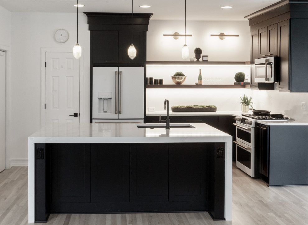 Foto på ett mellanstort funkis vit kök, med en undermonterad diskho, skåp i shakerstil, svarta skåp, bänkskiva i kvarts, vitt stänkskydd, vita vitvaror, ljust trägolv, en köksö och brunt golv