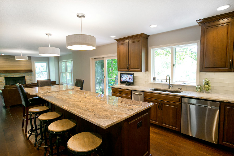 Example of a transitional l-shaped medium tone wood floor eat-in kitchen design with a double-bowl sink, raised-panel cabinets, dark wood cabinets, granite countertops, white backsplash, glass tile backsplash, stainless steel appliances and an island