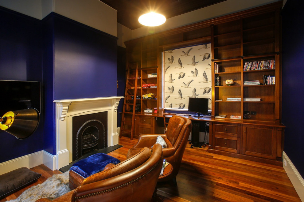 Inspiration for a mid-sized traditional study room in Other with blue walls, a standard fireplace, a plaster fireplace surround, a built-in desk, brown floor and medium hardwood floors.