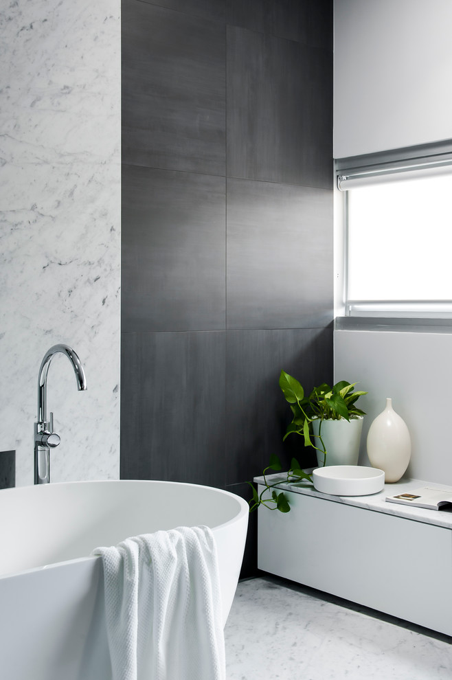 This is an example of a large contemporary master bathroom in Sydney with an integrated sink, furniture-like cabinets, white cabinets, solid surface benchtops, a freestanding tub, an open shower, a one-piece toilet, gray tile, ceramic tile, grey walls and ceramic floors.