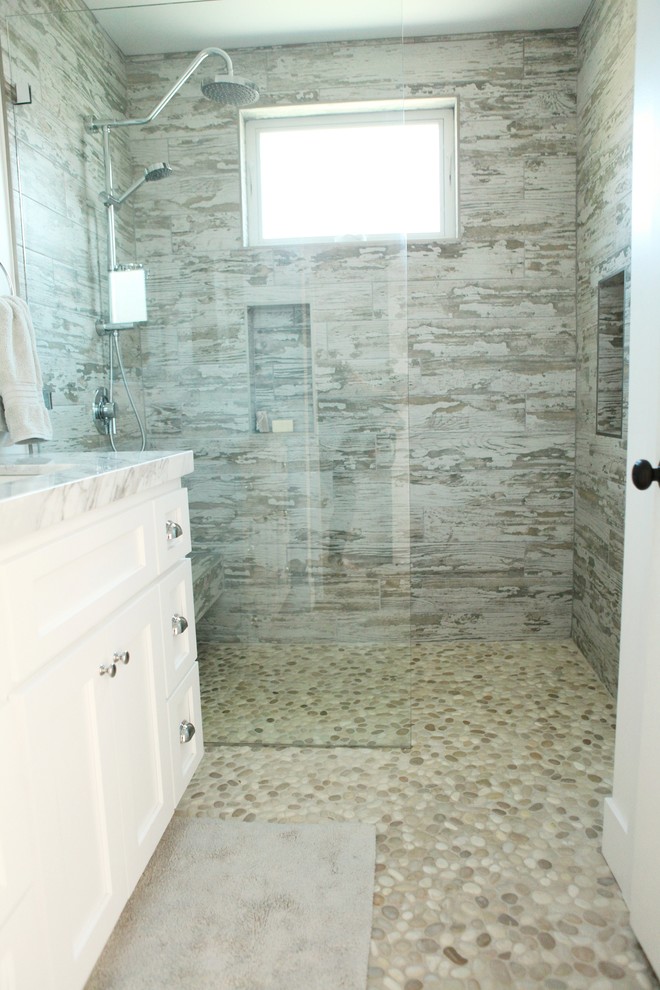 This is an example of a contemporary bathroom in Los Angeles with an undermount sink, shaker cabinets, white cabinets, marble benchtops, a curbless shower, gray tile, ceramic tile, white walls and pebble tile floors.