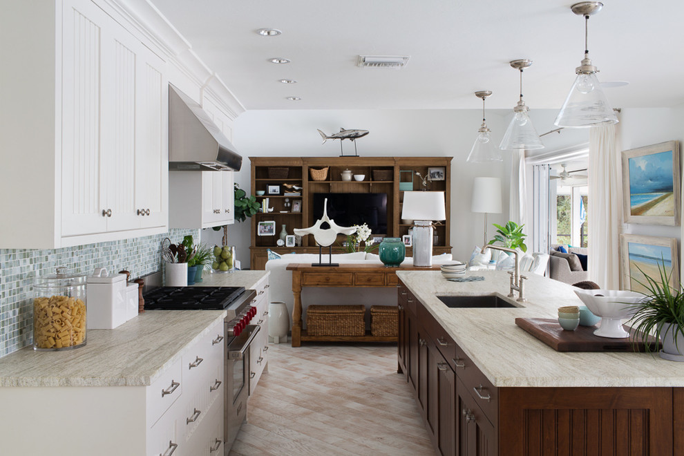 Large beach style galley open plan kitchen in Miami with an undermount sink, marble benchtops, multi-coloured splashback, stainless steel appliances, with island, light hardwood floors, recessed-panel cabinets, white cabinets and mosaic tile splashback.