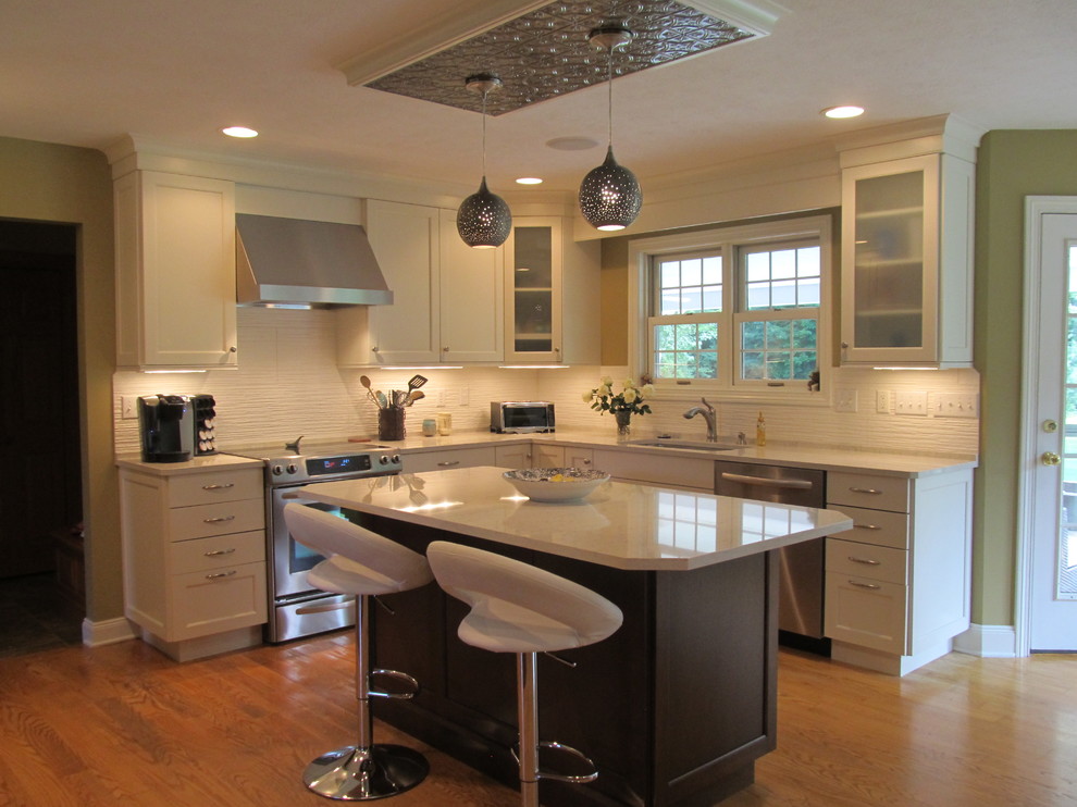 Example of a transitional l-shaped medium tone wood floor open concept kitchen design with an undermount sink, recessed-panel cabinets, white cabinets, quartz countertops, white backsplash, ceramic backsplash, stainless steel appliances and an island