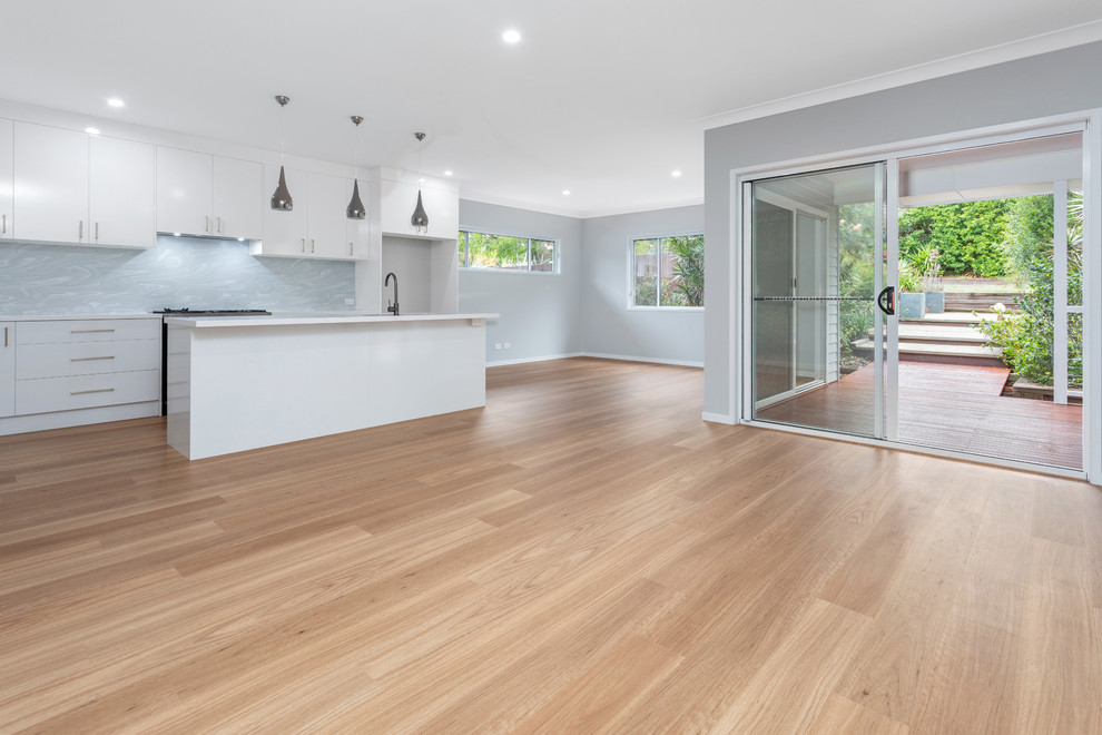 This is an example of a mid-sized contemporary galley kitchen pantry in Brisbane with an undermount sink, white cabinets, solid surface benchtops, grey splashback, black appliances, vinyl floors, with island, brown floor and white benchtop.