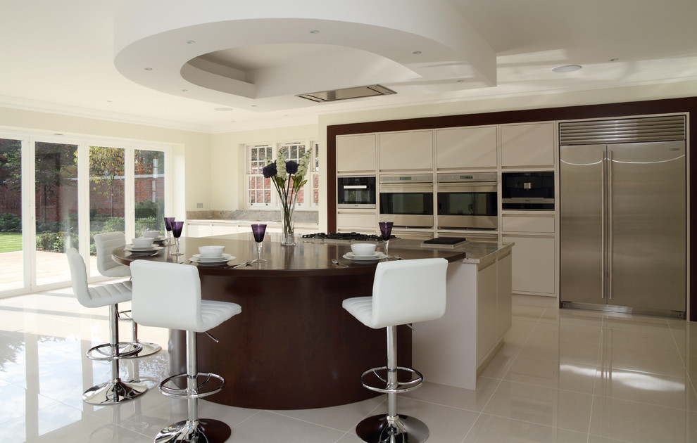 This is an example of a large contemporary kitchen in Hertfordshire with flat-panel cabinets, beige cabinets, stainless steel appliances, with island and beige floor.