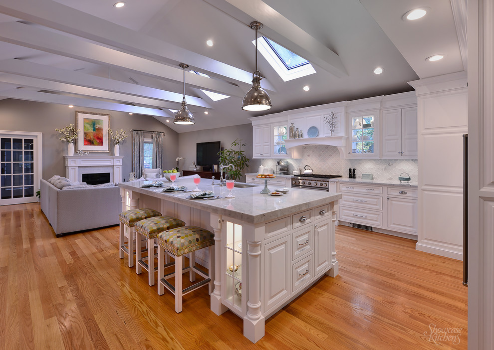 This is an example of a large transitional l-shaped open plan kitchen in New York with an undermount sink, shaker cabinets, white cabinets, marble benchtops, blue splashback, glass tile splashback, stainless steel appliances, light hardwood floors and with island.