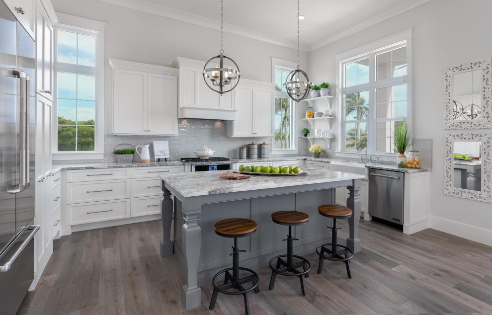 Design ideas for a large beach style u-shaped open plan kitchen in Tampa with a farmhouse sink, shaker cabinets, white cabinets, marble benchtops, white splashback, ceramic splashback, stainless steel appliances, medium hardwood floors, with island, brown floor, grey benchtop and vaulted.