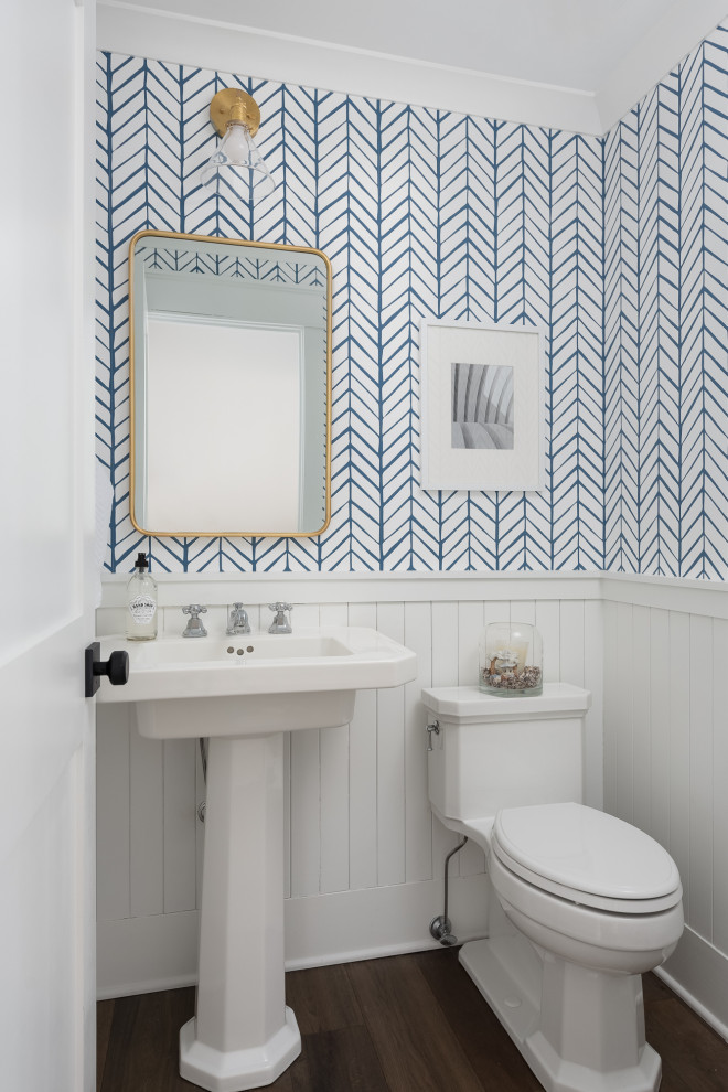 Inspiration for a small country powder room in Chicago with white cabinets, a one-piece toilet, white walls, medium hardwood floors, a pedestal sink, brown floor, a freestanding vanity and wallpaper.