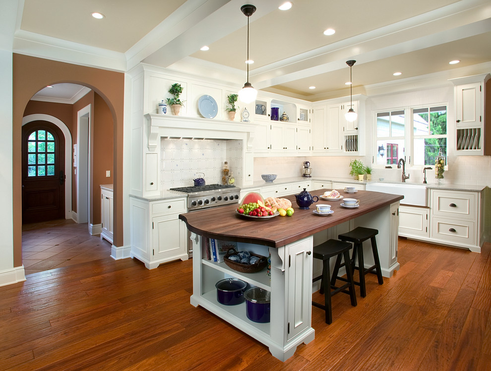 Design ideas for a large traditional l-shaped eat-in kitchen in Grand Rapids with a farmhouse sink, wood benchtops, recessed-panel cabinets, white cabinets, white splashback, stainless steel appliances, medium hardwood floors and with island.