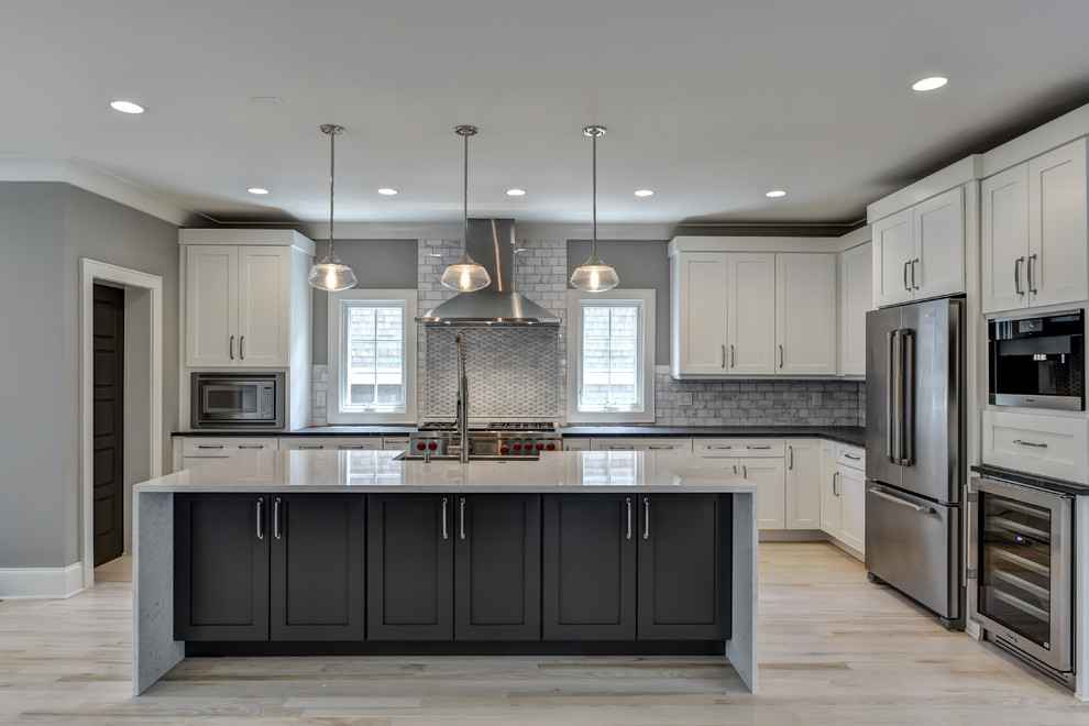 Kitchen - large contemporary l-shaped light wood floor kitchen idea in Atlanta with a farmhouse sink, shaker cabinets, white cabinets, soapstone countertops, gray backsplash, stone tile backsplash, stainless steel appliances and an island