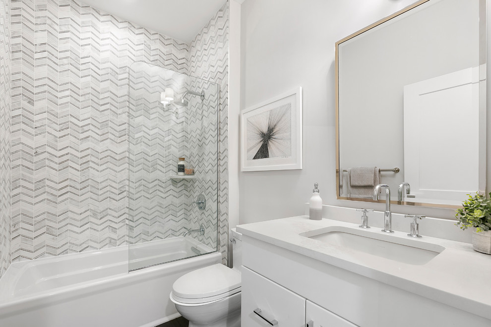 Inspiration for a transitional master bathroom in New York with a shower/bathtub combo, gray tile, grey walls, marble floors, an undermount sink, engineered quartz benchtops, a hinged shower door and white benchtops.