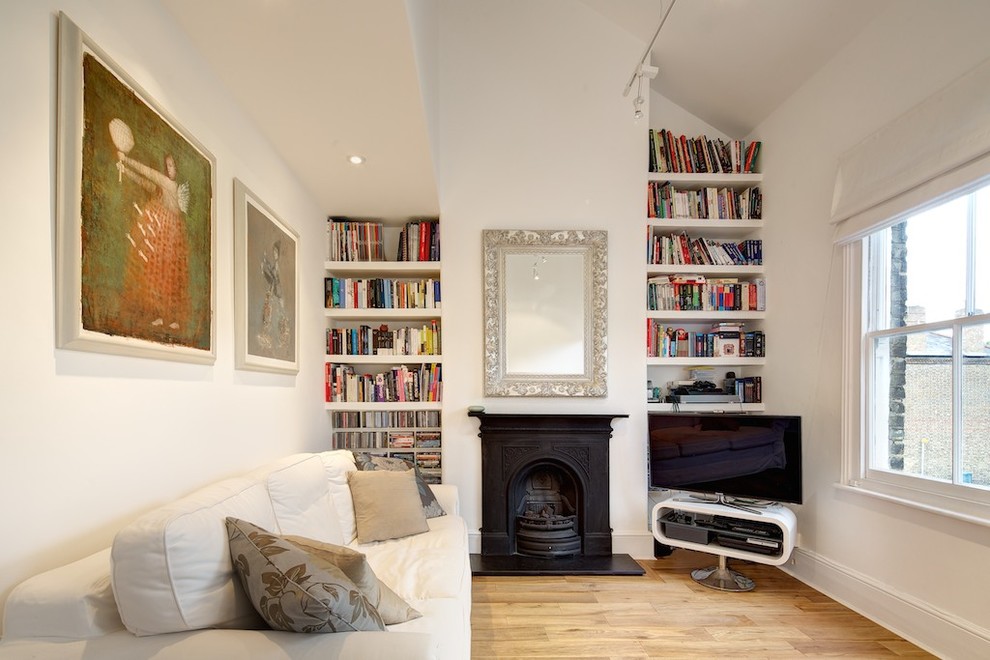 This is an example of a transitional living room in London with white walls, a freestanding tv, light hardwood floors and a standard fireplace.