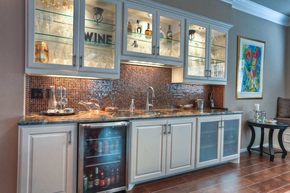 Design ideas for a mid-sized traditional single-wall wet bar in Houston with an undermount sink, glass-front cabinets, white cabinets, granite benchtops, brown splashback, glass tile splashback and dark hardwood floors.