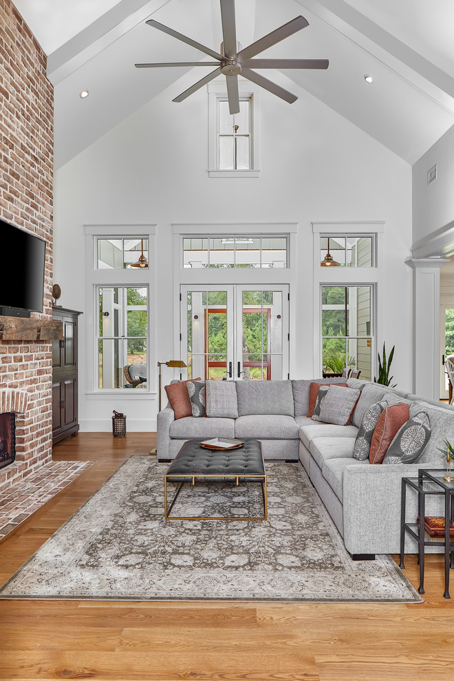 Living room - large coastal open concept light wood floor and brown floor living room idea in Charleston with white walls, a brick fireplace, a wall-mounted tv and a standard fireplace