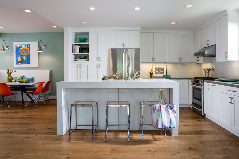 Inspiration for a mid-sized contemporary l-shaped eat-in kitchen in Los Angeles with white cabinets, light hardwood floors, with island, a double-bowl sink, shaker cabinets, quartzite benchtops, white splashback, subway tile splashback and stainless steel appliances.