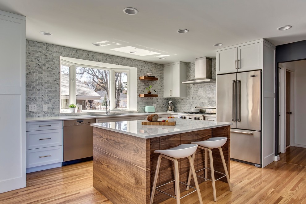 Transitional l-shaped medium tone wood floor and brown floor kitchen photo in Calgary with an undermount sink, shaker cabinets, white cabinets, gray backsplash, marble backsplash, stainless steel appliances, an island and white countertops