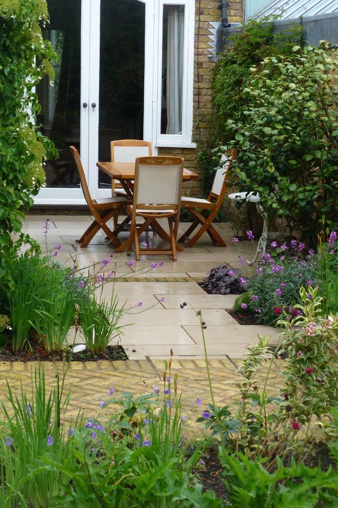 This is an example of a small traditional backyard patio in London with natural stone pavers.