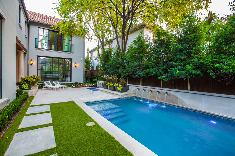 This is an example of a large mediterranean backyard rectangular lap pool in Dallas with a water feature and natural stone pavers.