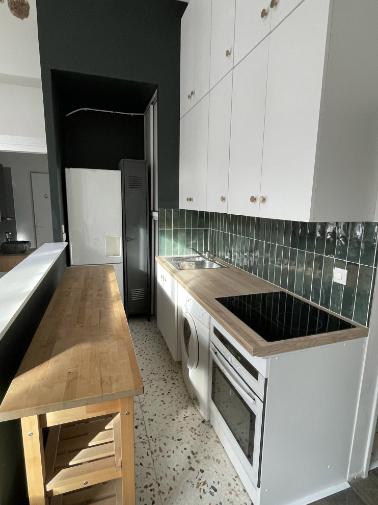 Foto på ett mellanstort funkis brun linjärt kök och matrum, med en dubbel diskho, vita skåp, laminatbänkskiva, grönt stänkskydd, stänkskydd i keramik, rostfria vitvaror, terrazzogolv och en köksö