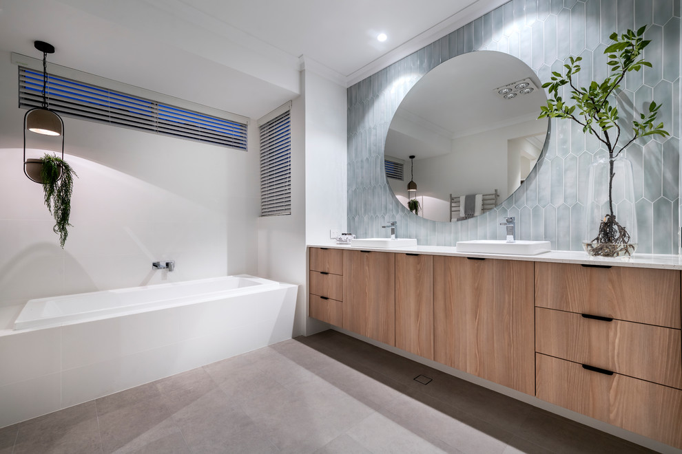 This is an example of a contemporary master bathroom in Perth with flat-panel cabinets, medium wood cabinets, a drop-in tub, gray tile, white walls, a drop-in sink, grey floor and white benchtops.