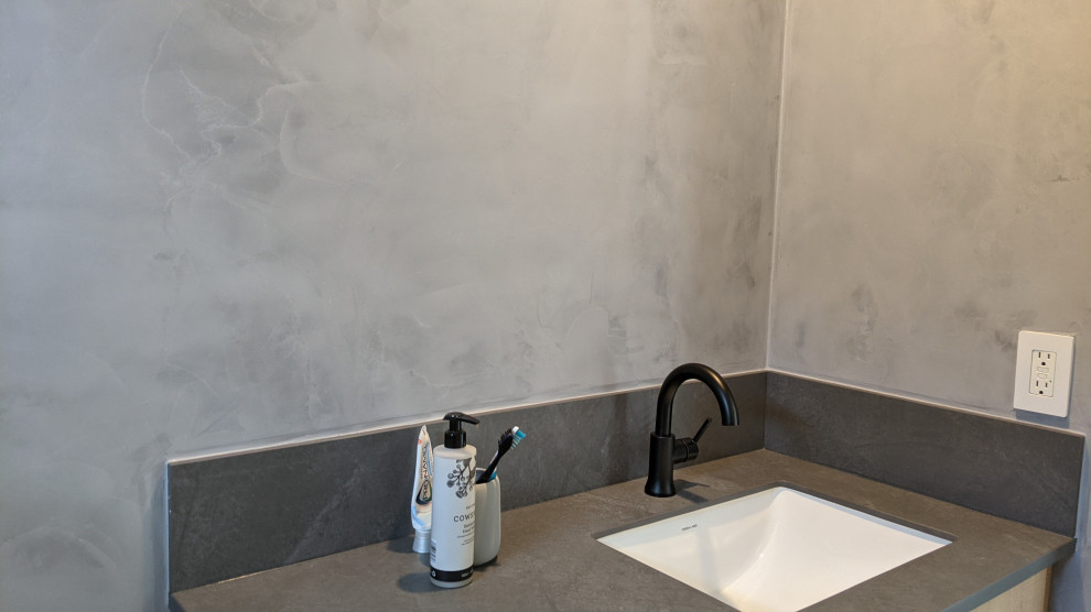 Foto på ett litet funkis grå badrum med dusch, med luckor med upphöjd panel, skåp i ljust trä, grå väggar och bänkskiva i kvarts