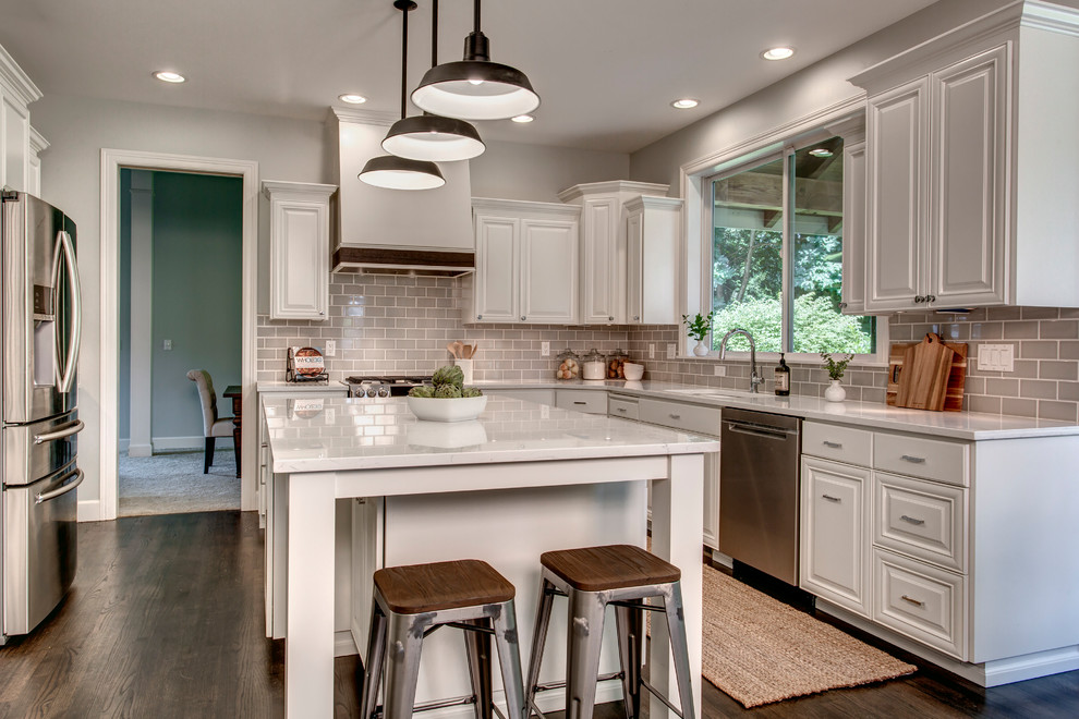 Large transitional u-shaped dark wood floor and brown floor eat-in kitchen photo in Seattle with an undermount sink, raised-panel cabinets, white cabinets, marble countertops, gray backsplash, ceramic backsplash, stainless steel appliances and an island