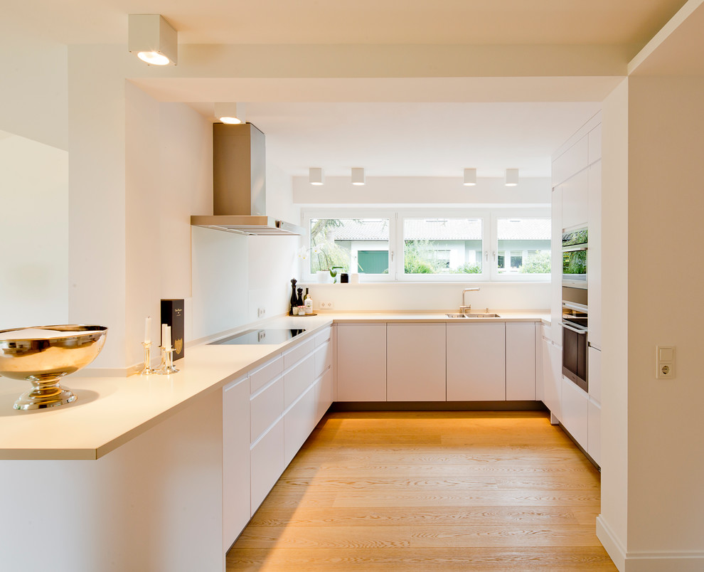 Inspiration for a contemporary u-shaped separate kitchen in Dusseldorf with an undermount sink, flat-panel cabinets, white cabinets, white splashback, glass sheet splashback, panelled appliances, light hardwood floors and no island.