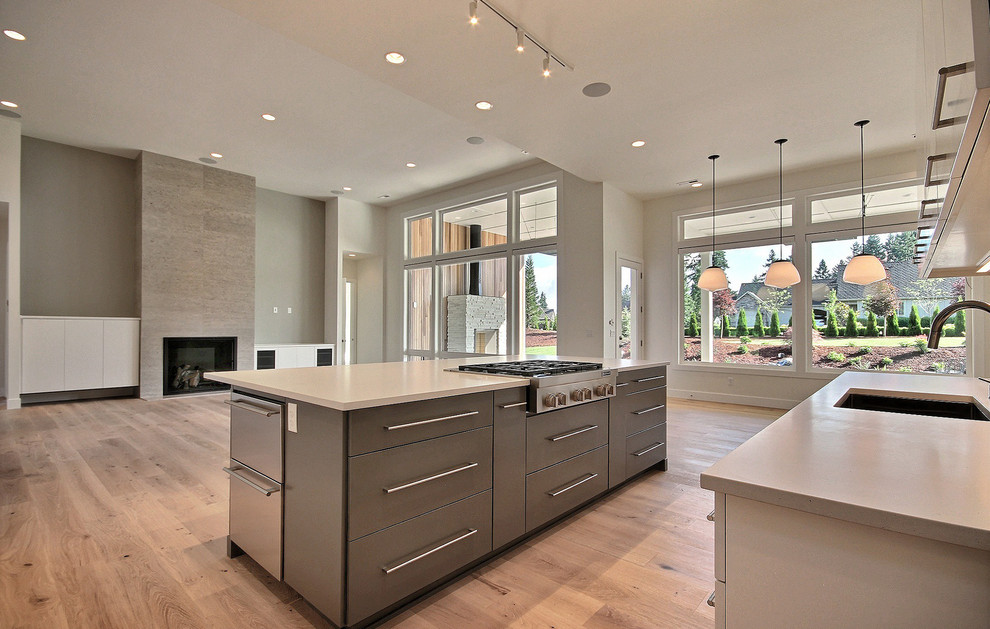 This is an example of an expansive modern u-shaped open plan kitchen in Portland with an undermount sink, flat-panel cabinets, white cabinets, quartz benchtops, grey splashback, glass tile splashback, stainless steel appliances, light hardwood floors, with island, brown floor and grey benchtop.