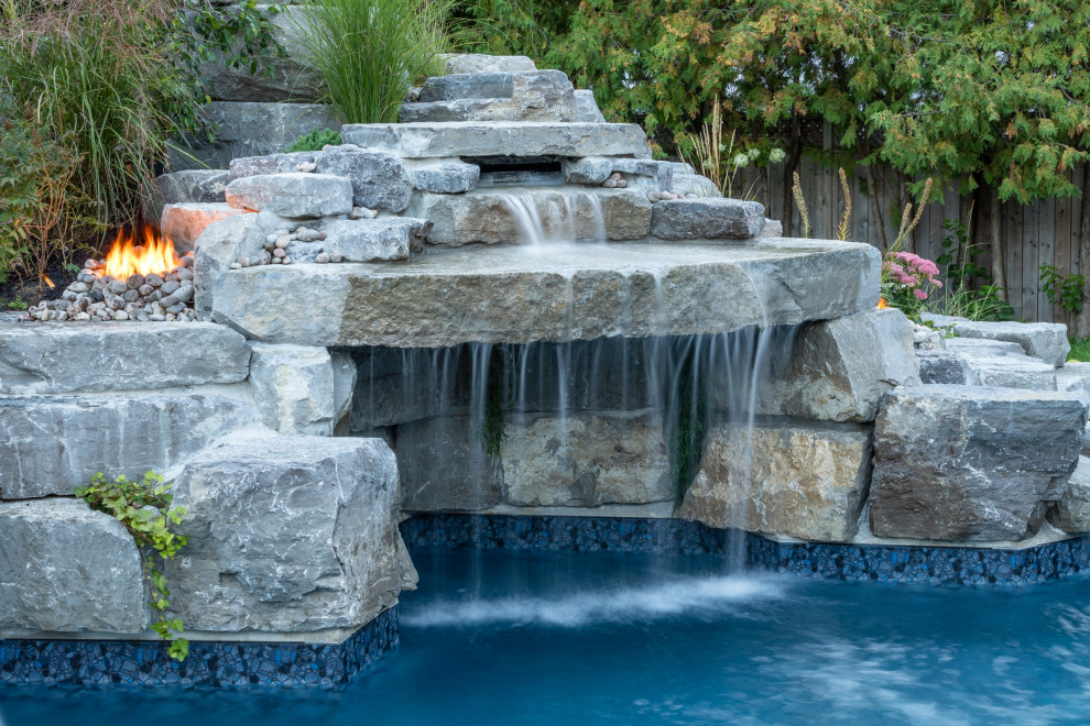 Design ideas for a mid-sized transitional backyard custom-shaped natural pool in Toronto with a water feature and stamped concrete.