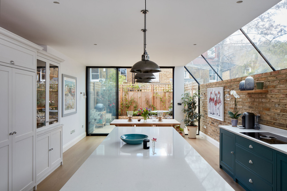 Medium sized contemporary single-wall kitchen/diner in London with a built-in sink, shaker cabinets, blue cabinets, composite countertops, brown splashback, brick splashback, integrated appliances, medium hardwood flooring, an island, brown floors and white worktops.