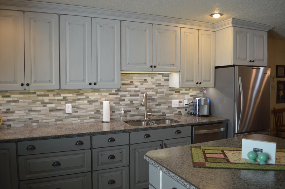 Example of a small transitional l-shaped eat-in kitchen design with raised-panel cabinets, white cabinets, quartzite countertops, gray backsplash, porcelain backsplash, stainless steel appliances, an island, gray countertops and an undermount sink