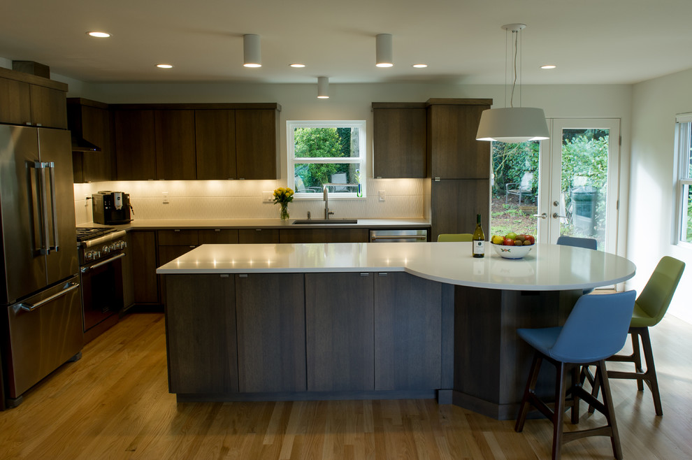 Design ideas for a large modern l-shaped open plan kitchen in Portland with a drop-in sink, flat-panel cabinets, dark wood cabinets, quartzite benchtops, white splashback, subway tile splashback, stainless steel appliances, light hardwood floors, with island and brown floor.