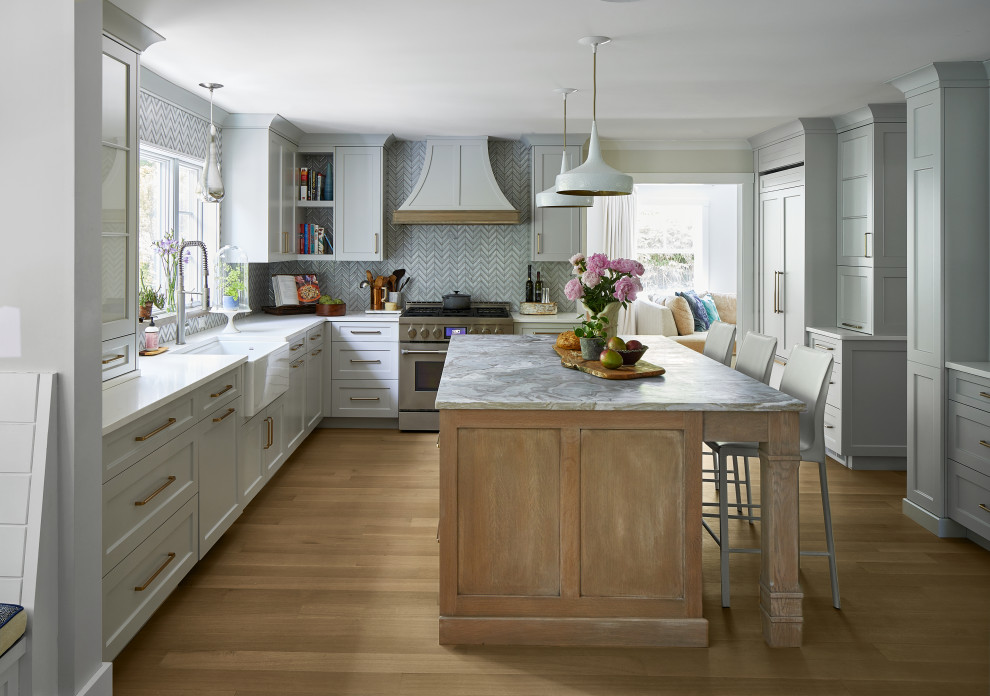 Design ideas for a medium sized classic kitchen in New York with a belfast sink, grey cabinets, granite worktops, grey splashback, stainless steel appliances, light hardwood flooring, an island, brown floors and white worktops.