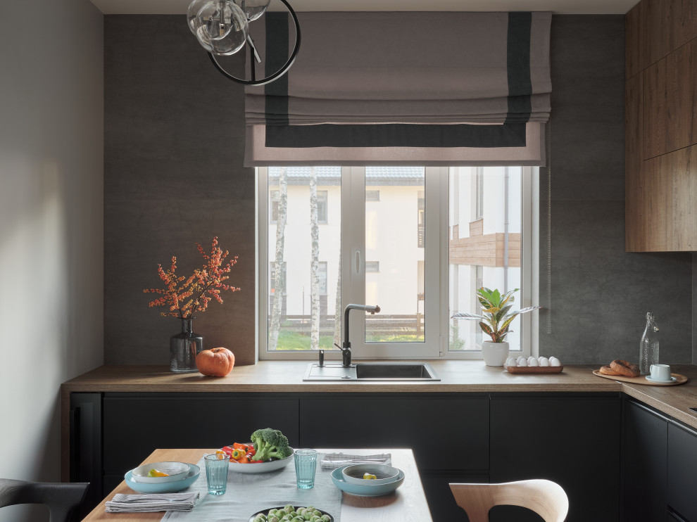 Photo of a mid-sized contemporary l-shaped eat-in kitchen in Saint Petersburg with a drop-in sink, flat-panel cabinets, black cabinets, wood benchtops, grey splashback, porcelain splashback, black appliances, porcelain floors, no island, brown floor and beige benchtop.