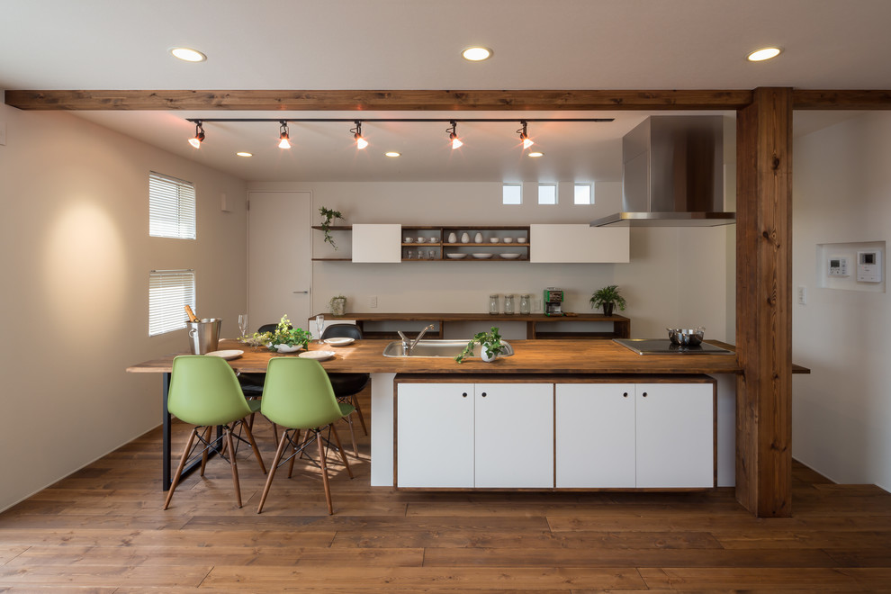 Inspiration for an asian galley eat-in kitchen in Other with a drop-in sink, flat-panel cabinets, white cabinets, wood benchtops, white splashback, stainless steel appliances, medium hardwood floors, with island and brown floor.